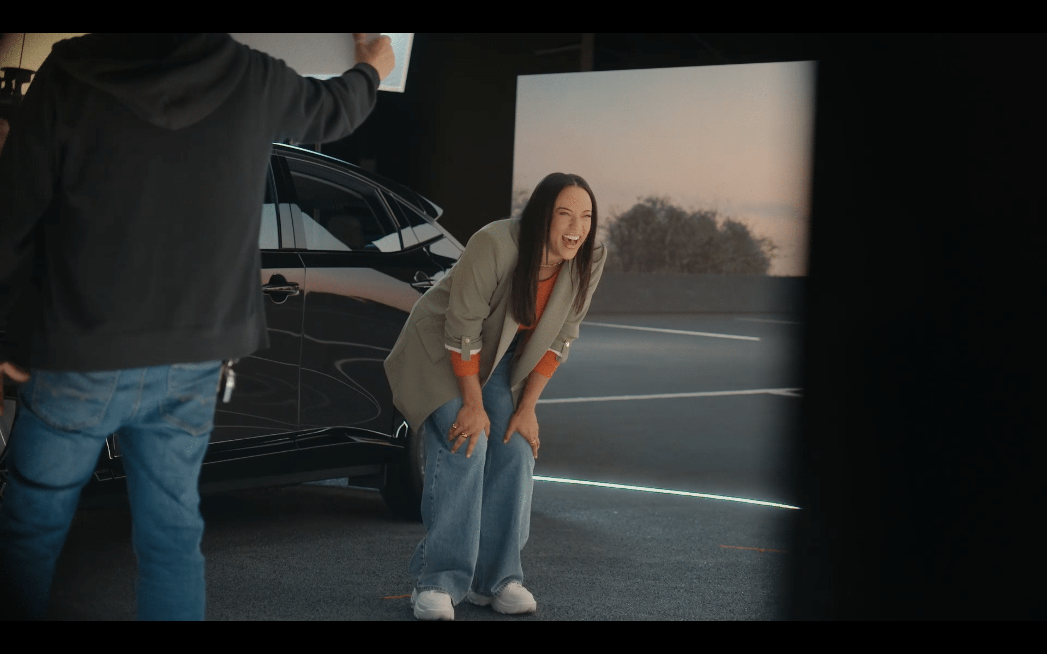 A person laughing during the filming of the Nissan ARIYA experience, standing next to the electric vehicle